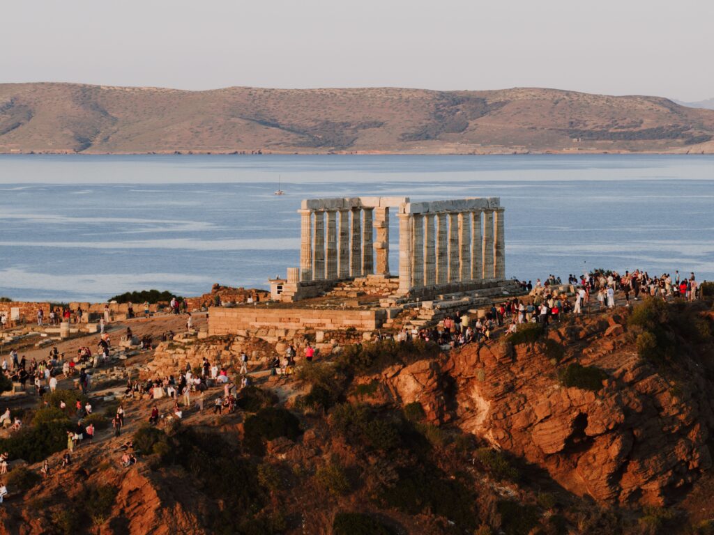 A breathtaking view of the Temple of Poseidon in Sounion with a crowd gathering at sunset.