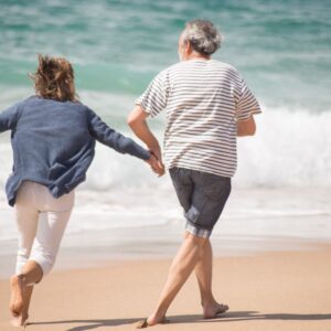 Senior couple holding hands and running by the ocean at a Portuguese beach during the day.