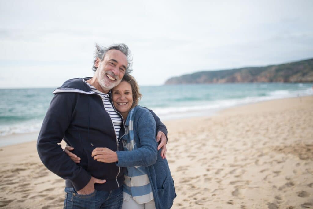 Happy senior couple embracing on a sandy beach in Portugal, symbolizing love and togetherness.
